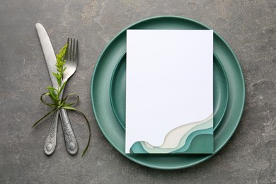 Photo of Empty menu, plates, cutlery and floral decor on grey table, top view. Mockup for design