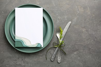 Photo of Empty menu, plates, cutlery and floral decor on grey table, top view. Mockup for design