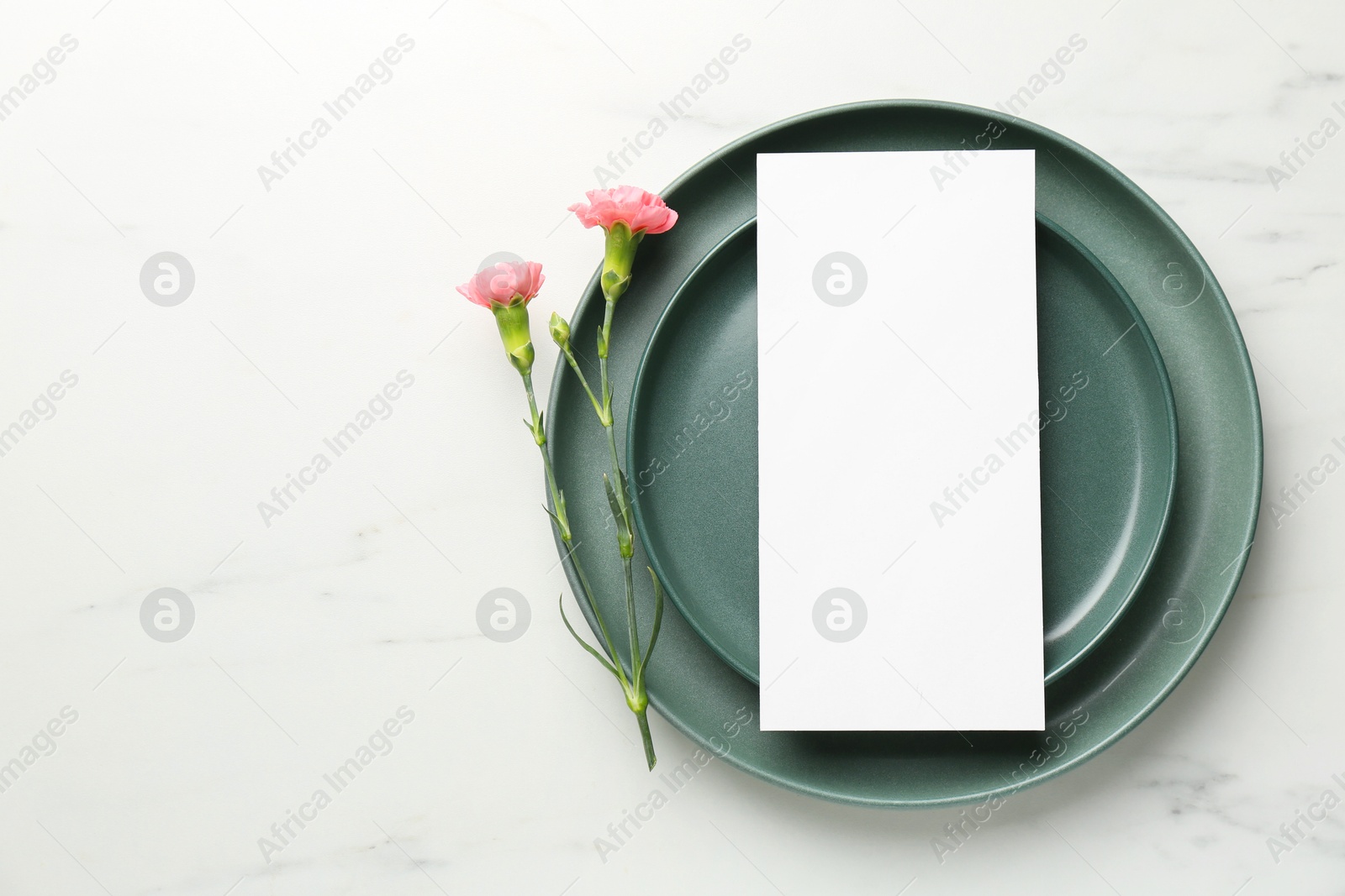 Photo of Empty menu, plates and floral decor on white marble table, top view. Mockup for design