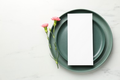 Photo of Empty menu, plates and floral decor on white marble table, top view. Mockup for design