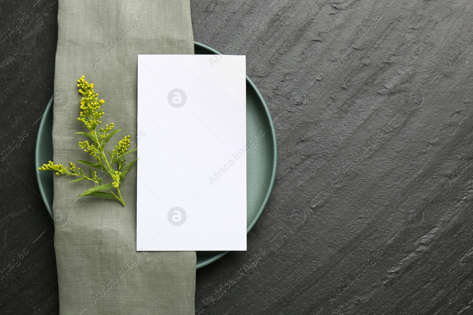 Photo of Empty menu, plate, napkin and floral decor on black table, top view. Mockup for design