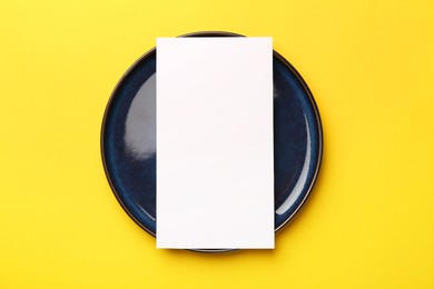 Photo of Empty menu and plate on yellow background, top view. Mockup for design