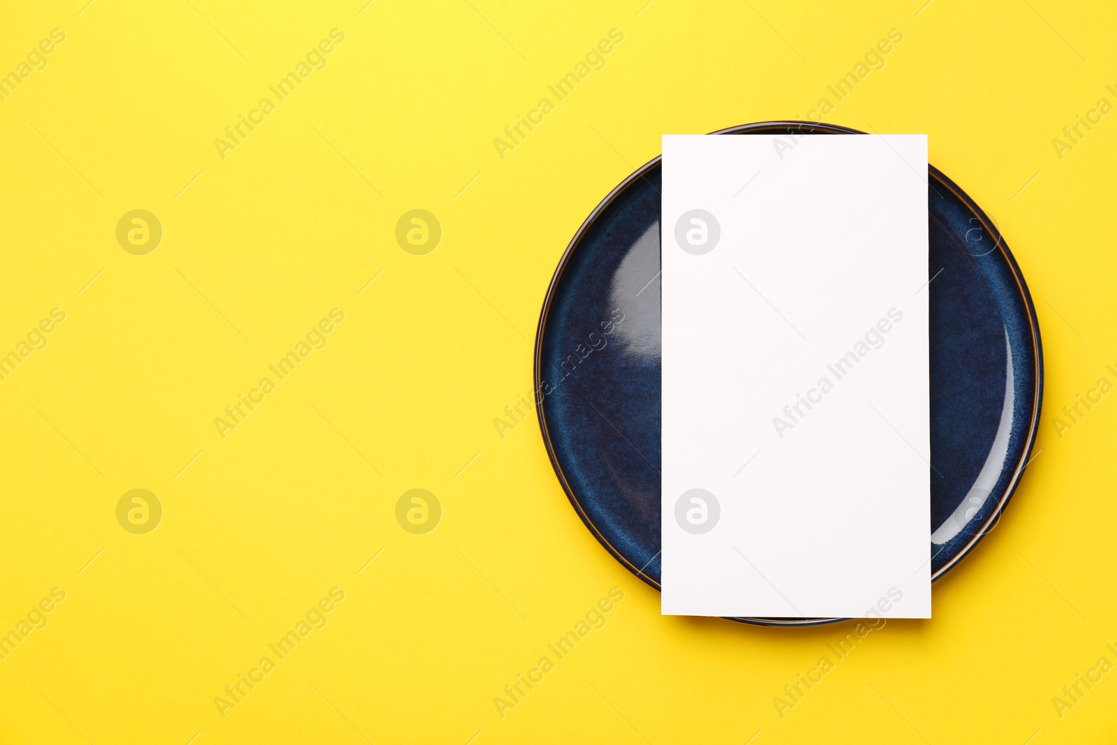 Photo of Empty menu and plate on yellow background, top view. Mockup for design