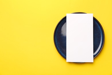 Photo of Empty menu and plate on yellow background, top view. Mockup for design