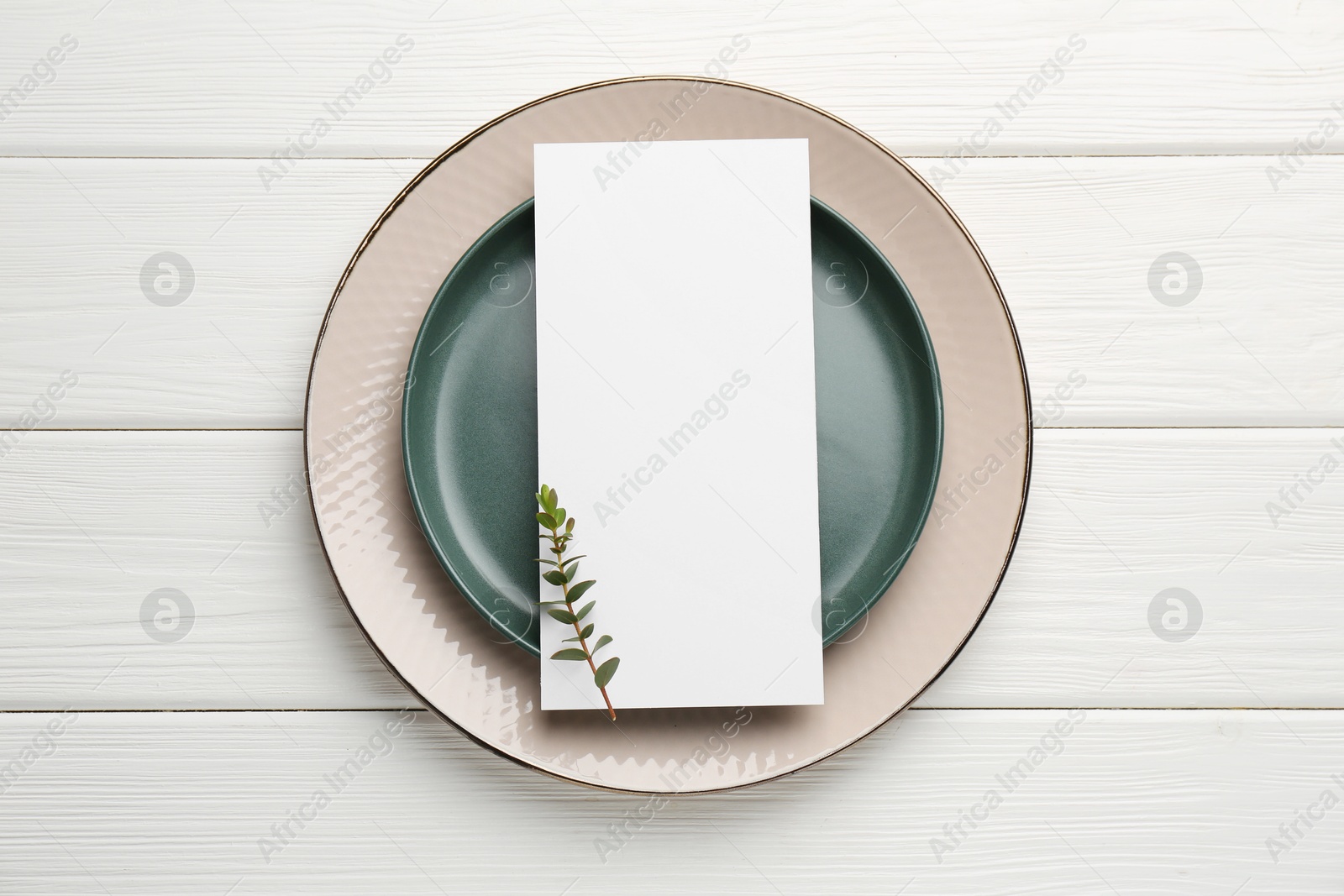 Photo of Empty menu, plates and floral decor on white wooden table, top view. Mockup for design