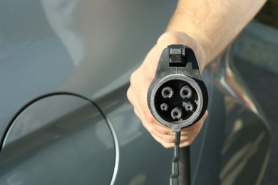 Photo of Man holding power supply cable near car at electric vehicle charging station, closeup