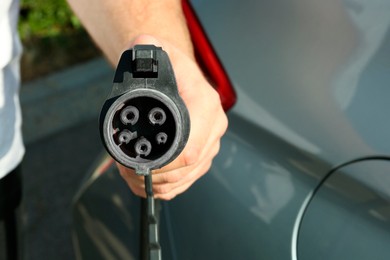 Photo of Man holding power supply cable near car at electric vehicle charging station, closeup