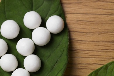 Homeopathy. Many pills and green leaves on wooden table, flat lay