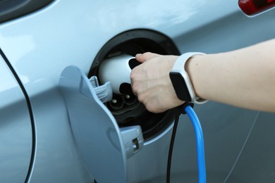 Woman inserting plug into electric car socket at charging station outdoors, closeup