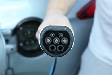 Photo of Man with power supply cable at electric car charging station outdoors, closeup