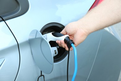 Photo of Man inserting plug into electric car socket at charging station outdoors, closeup