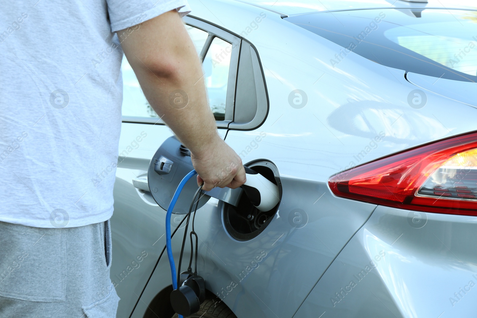 Photo of Man inserting plug into electric car socket at charging station outdoors, closeup