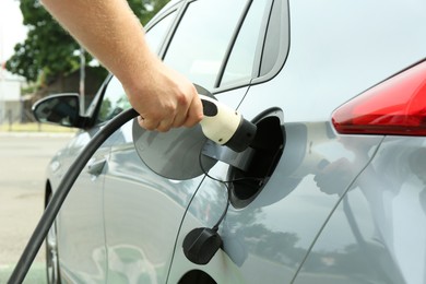 Photo of Man inserting plug into electric car socket at charging station outdoors, closeup