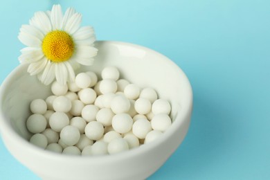 Photo of Homeopathy. Many pills and chamomile flower in bowl on light blue background, space for text