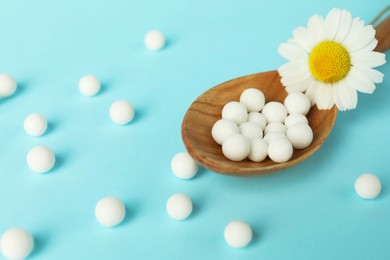 Photo of Homeopathy. Spoon with many pills and chamomile flower on light blue background