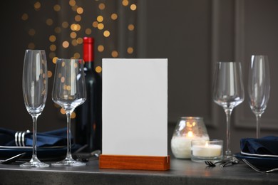 Menu holder, clean dishware and burning candles on gray table against blurred lights