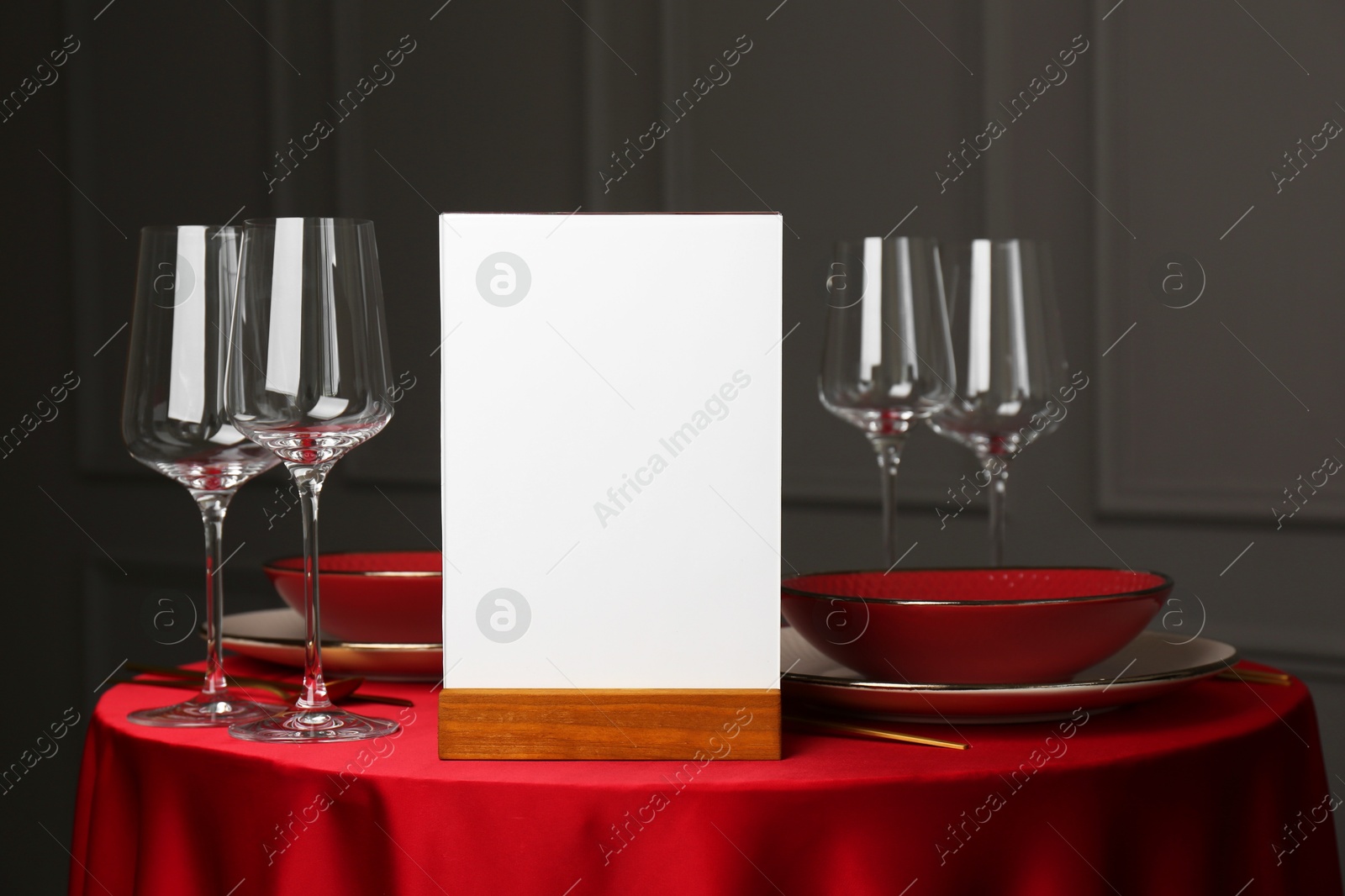 Photo of Menu holder, clean dishware and cutlery on red table in restaurant