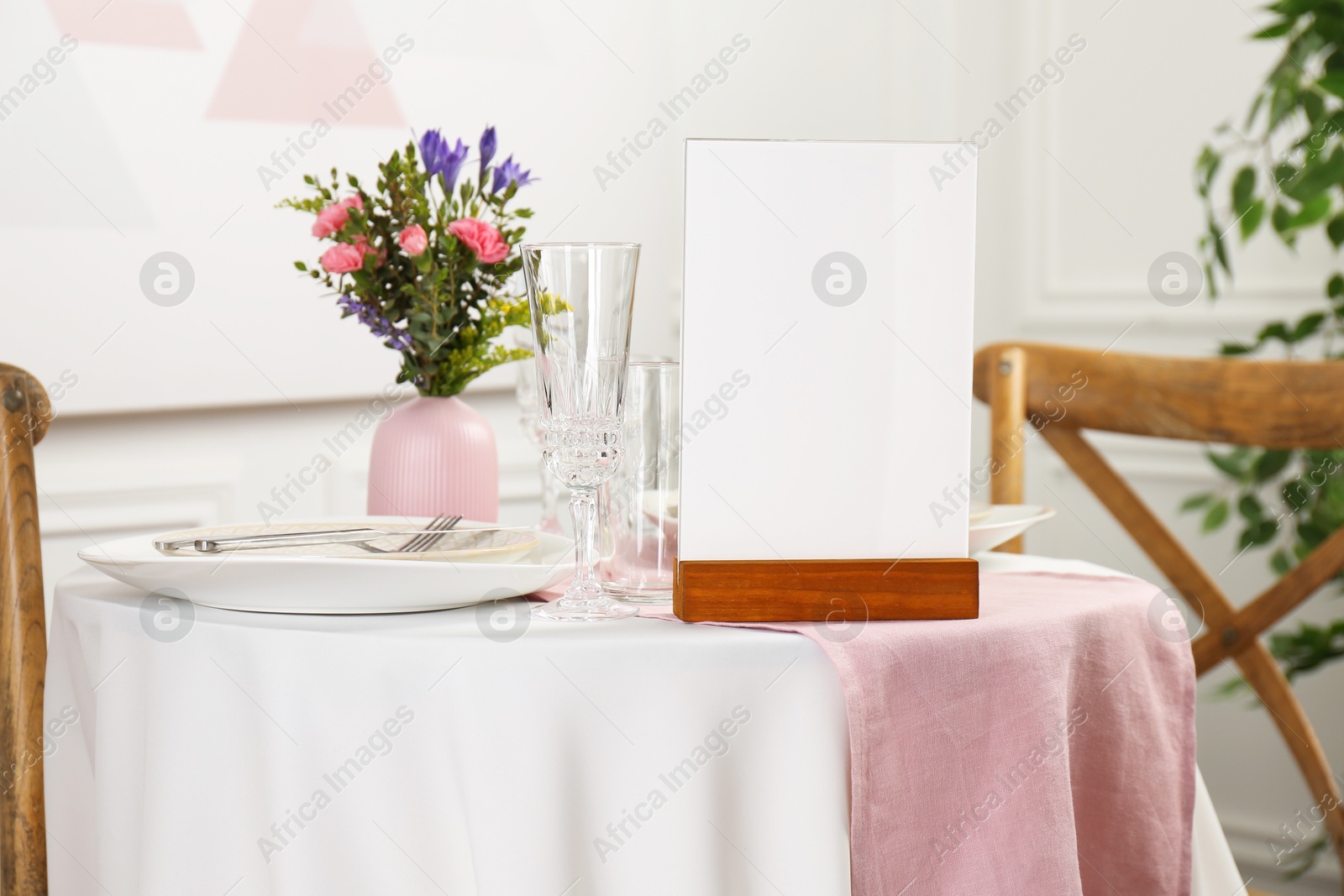 Photo of Menu holder, clean dishware and vase with beautiful flowers on white table in restaurant