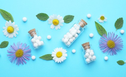 Homeopathy. Glass bottles, pills, flowers and green leaves on light blue background, flat lay