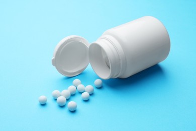 Photo of Homeopathy. Overturned plastic bottle and pills on light blue background