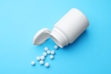 Photo of Homeopathy. Overturned plastic bottle and pills on light blue background