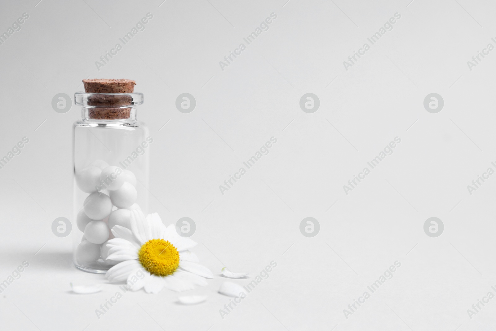 Photo of Homeopathy. Pills in glass bottle and chamomile on white background, space for text