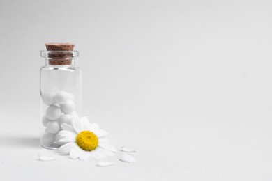 Homeopathy. Pills in glass bottle and chamomile on white background, space for text