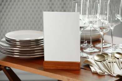 Photo of Menu holder, clean dishware and cutlery on wooden table indoors