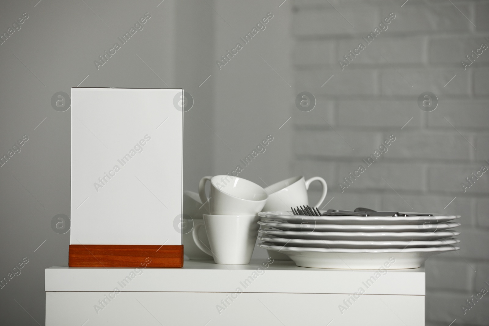 Photo of Menu holder and clean dishware on white table indoors