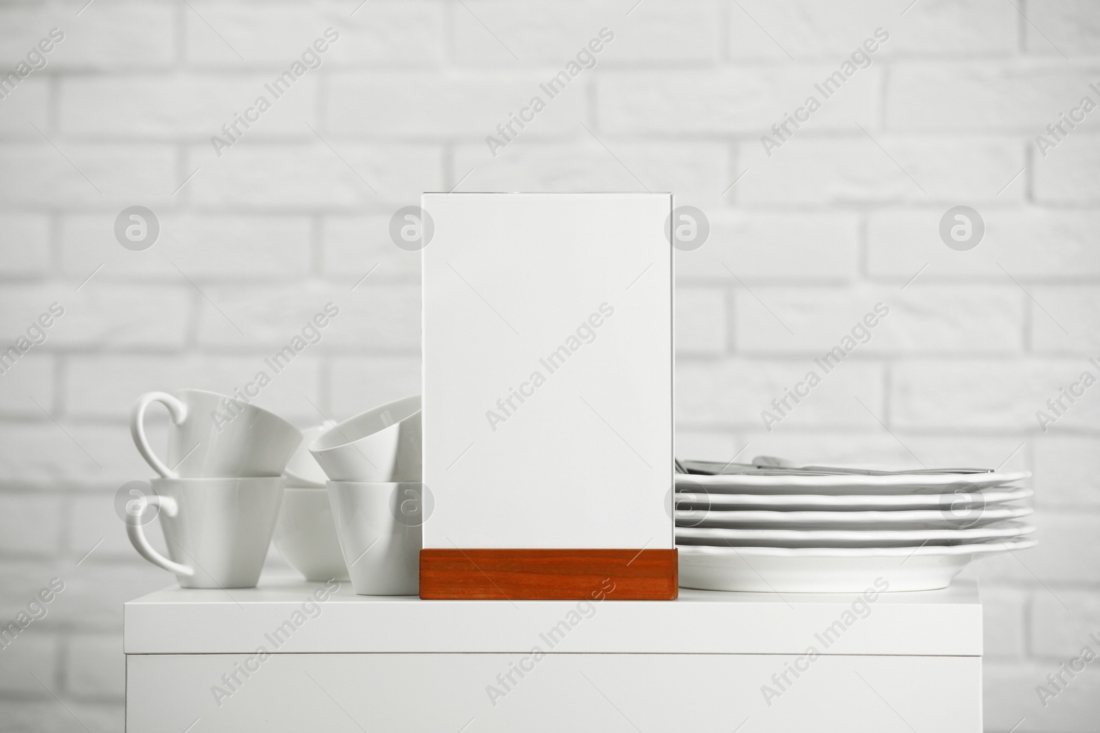 Photo of Menu holder and clean dishware on white table indoors