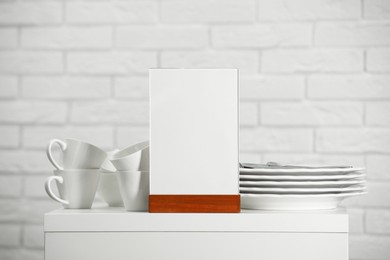 Photo of Menu holder and clean dishware on white table indoors