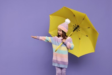 Cute little girl with yellow umbrella on purple background