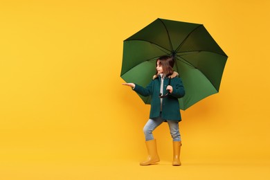 Photo of Cute little girl with green umbrella on yellow background. Space for text