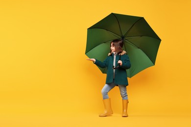 Cute little girl with green umbrella on yellow background. Space for text