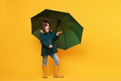 Photo of Cute little girl with green umbrella on yellow background