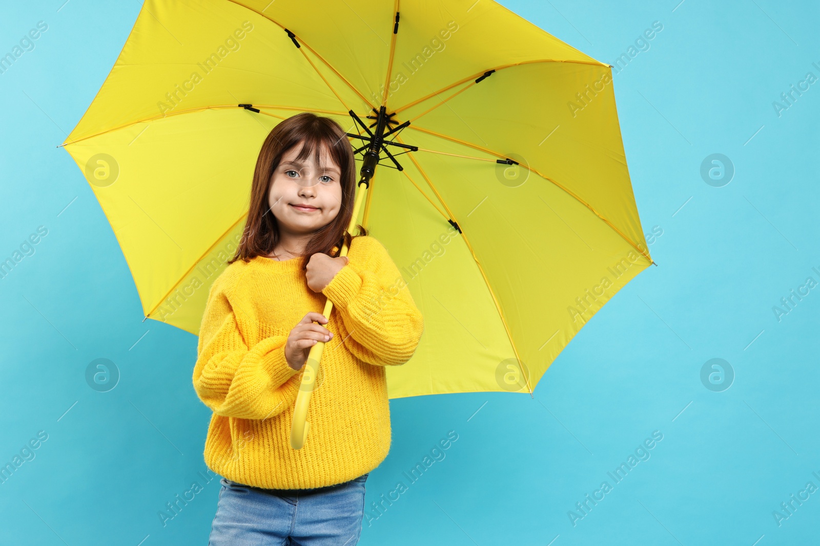 Photo of Cute little girl with yellow umbrella on light blue background