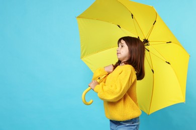 Photo of Cute little girl with yellow umbrella on light blue background. Space for text