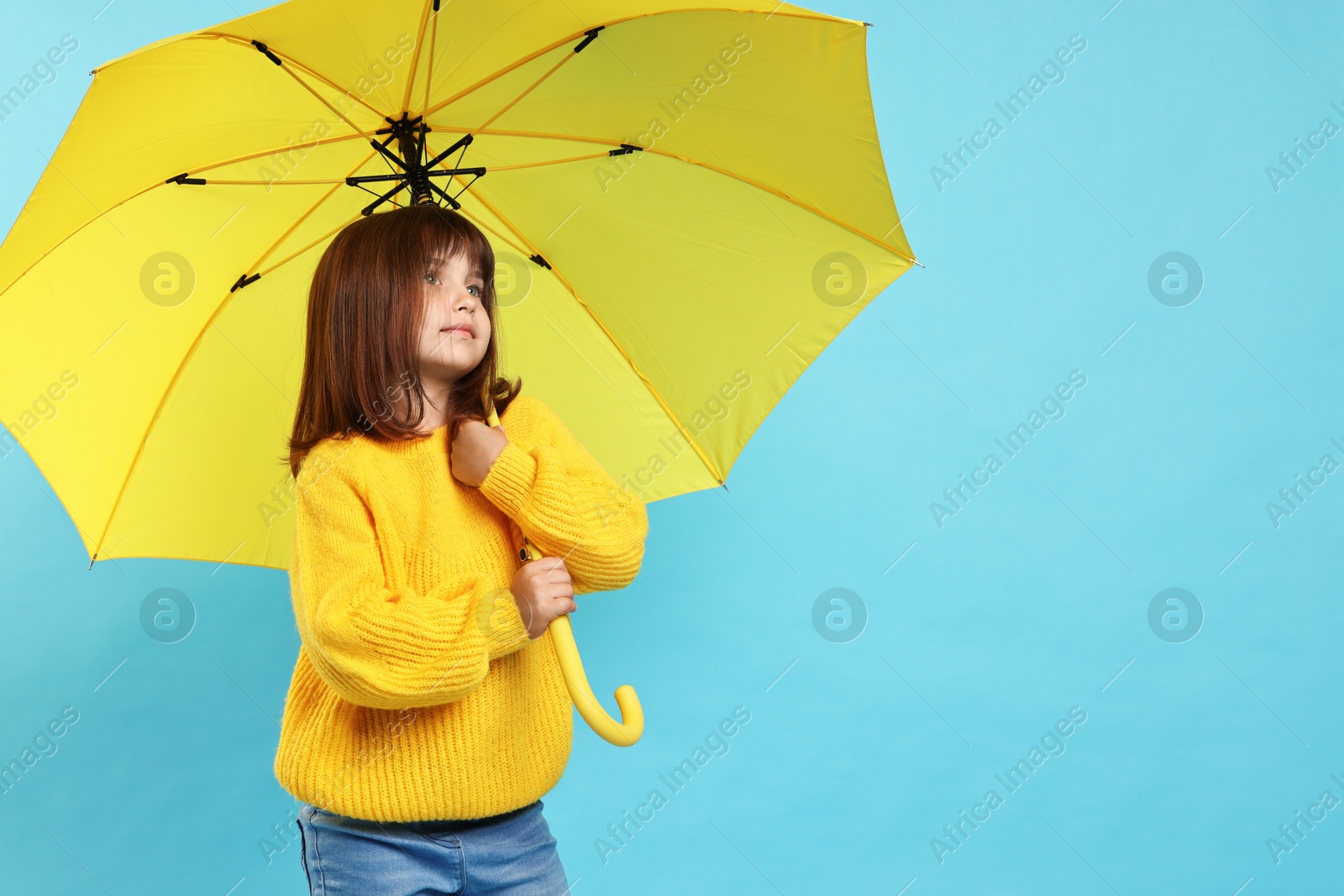 Photo of Cute little girl with yellow umbrella on light blue background. Space for text