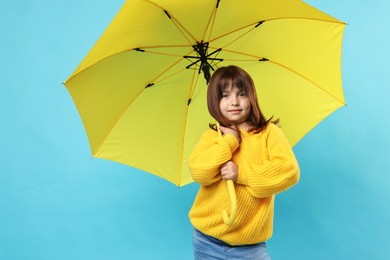 Photo of Cute little girl with yellow umbrella on light blue background