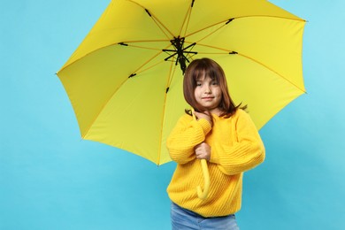 Cute little girl with yellow umbrella on light blue background