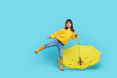 Photo of Cute little girl with yellow umbrella on light blue background