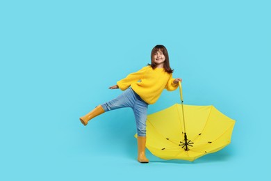 Cute little girl with yellow umbrella on light blue background