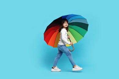 Photo of Cute little girl with colorful umbrella on light blue background