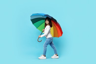 Photo of Cute little girl with colorful umbrella on light blue background