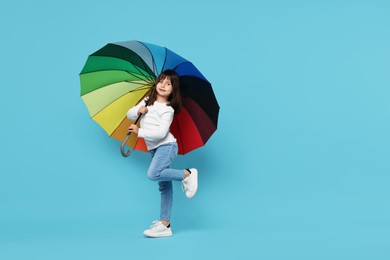 Photo of Cute little girl with colorful umbrella on light blue background. Space for text