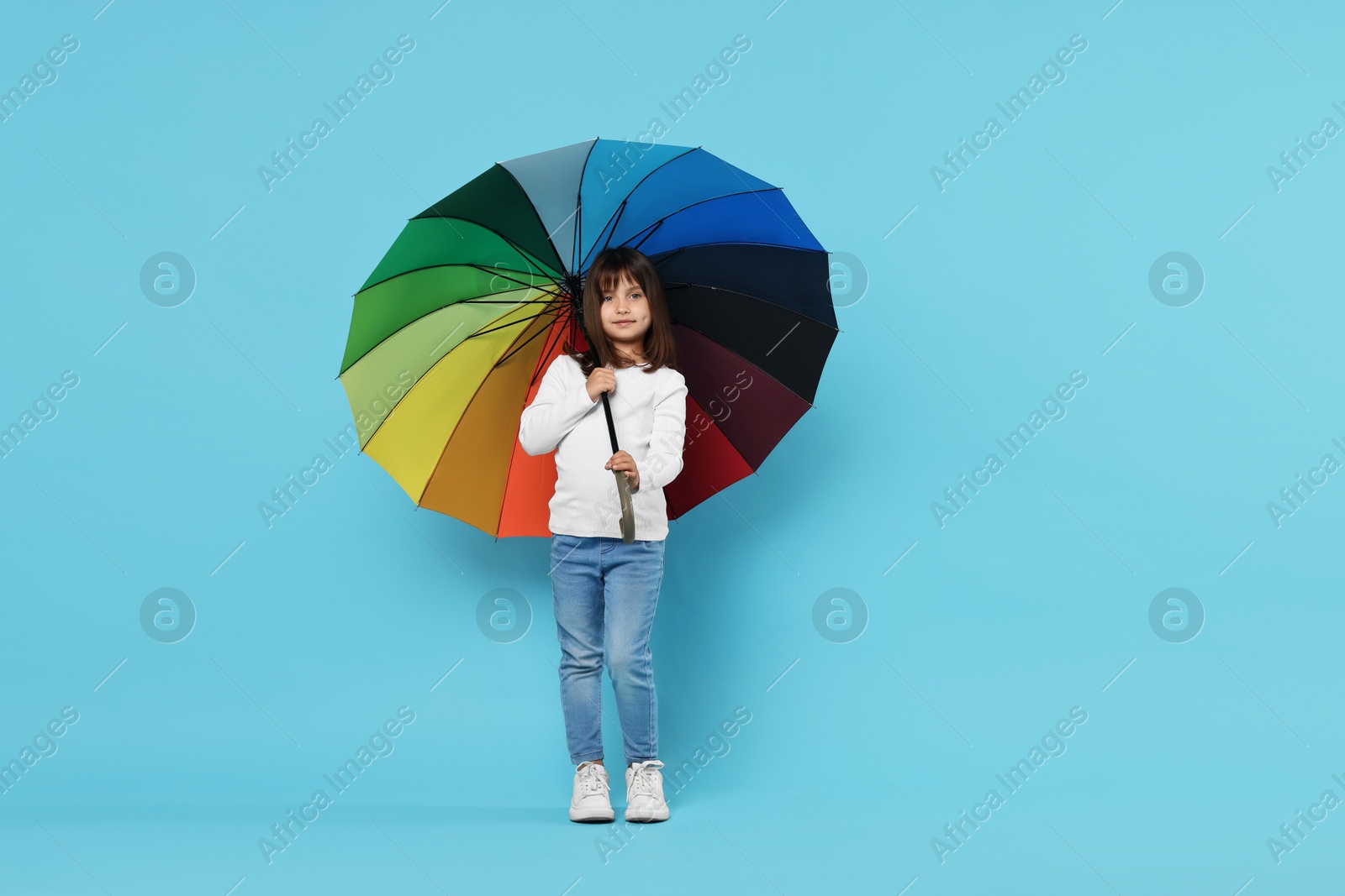 Photo of Cute little girl with colorful umbrella on light blue background