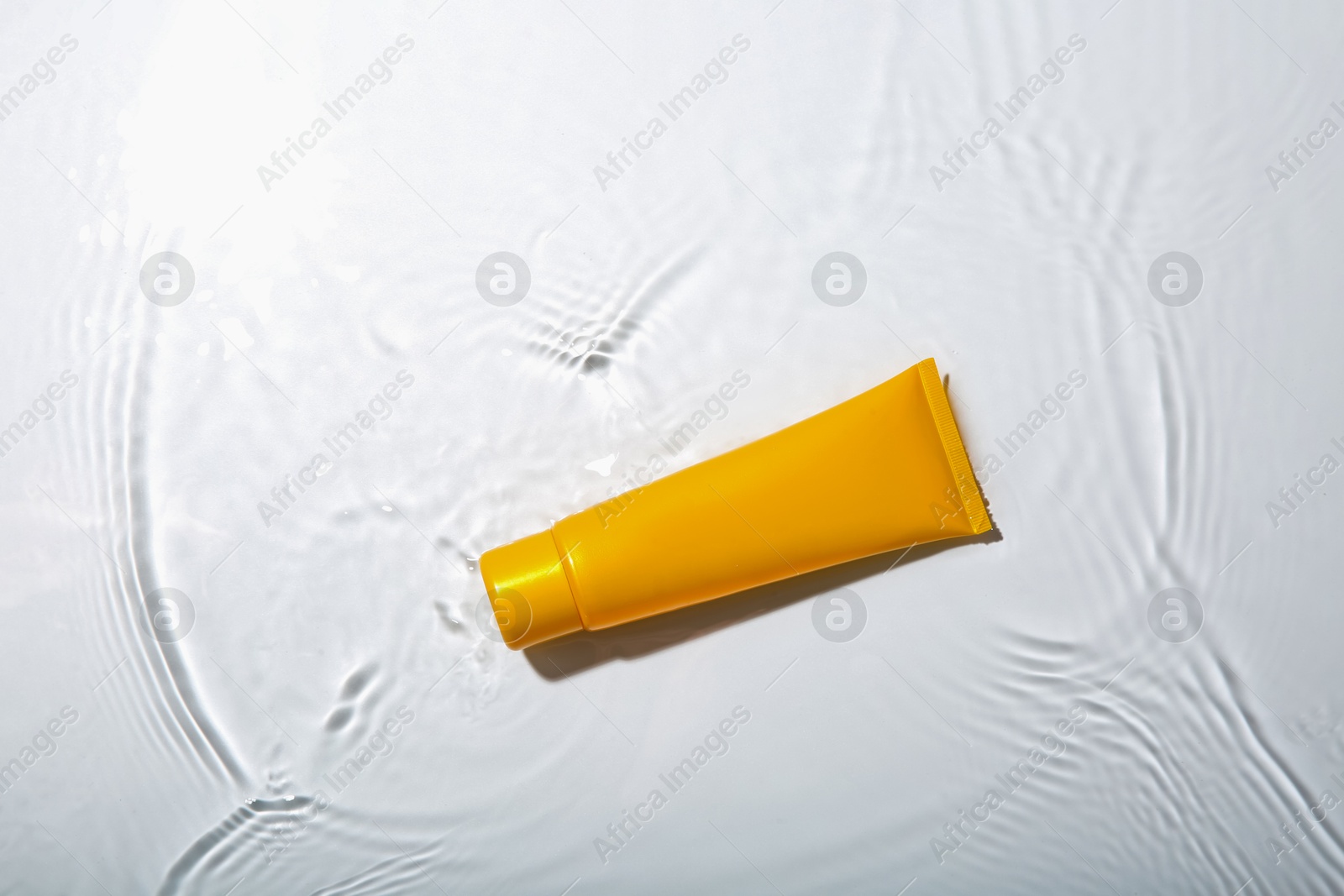 Photo of Cosmetic product. Tube with cream in water on light background, top view