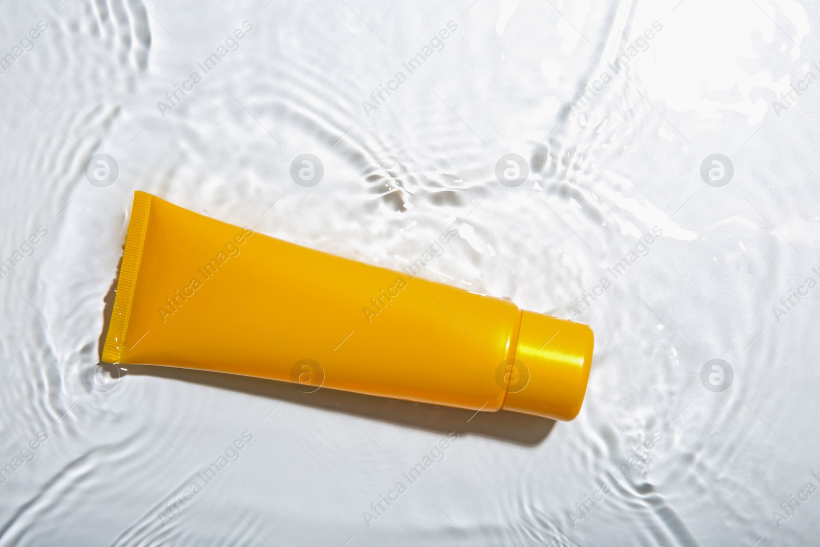 Photo of Cosmetic product. Tube with cream in water on light background, top view