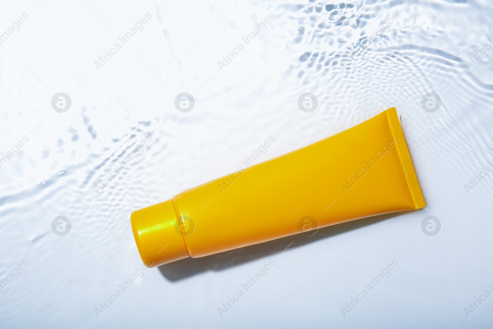 Photo of Cosmetic product. Tube with cream in water on light background, top view