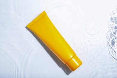 Photo of Cosmetic product. Tube with cream in water on light background, top view